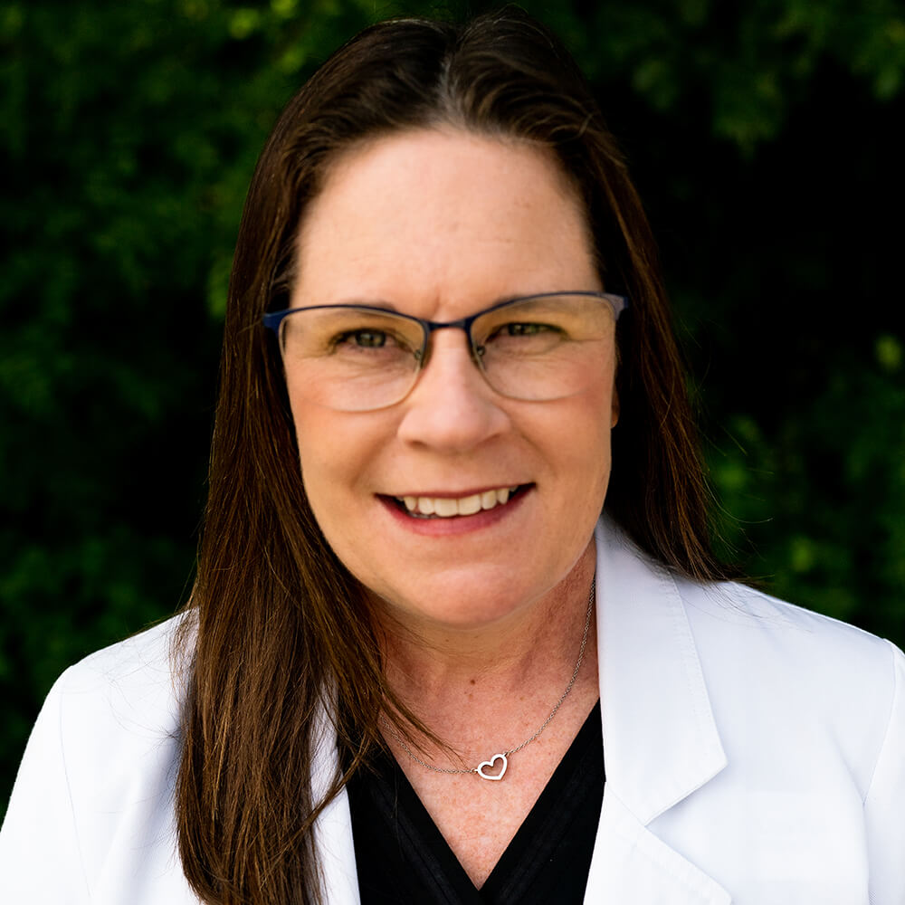 Dr. Lisa B. Fell wearing a white lab coat over a black shirt at Audiology Experts in Arlington, TX