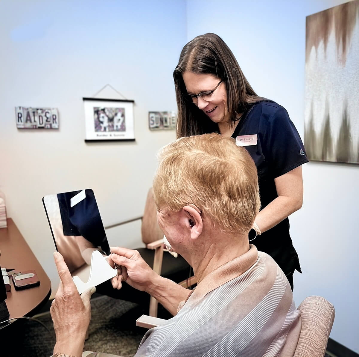 Dr. Lisa Fell with a patient looking at his hearing aids in a mirror at Audiology Experts in Arlington, TX.