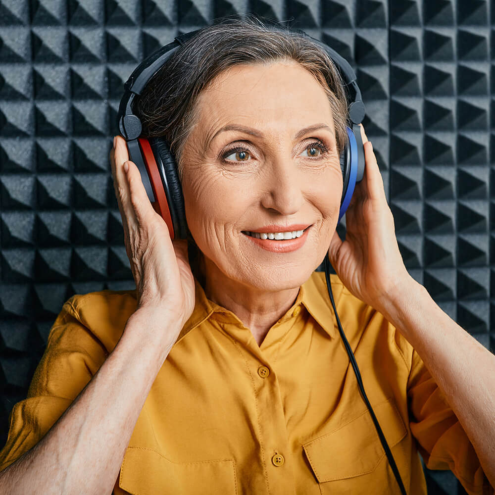 A happy woman with her hands holding headphones on her head.